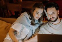 Why Is Illegal Streaming So Popular? 7 Reasons People Choose Piracy A couple sitting together at home, engaged with a laptop while watching a streaming website.