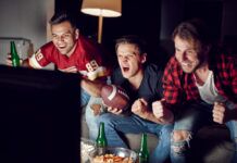 How To Watch Each Round of the 2024/25 NCAA College Football Playoffs Three excited men cheer for their team while watching a football match on television.