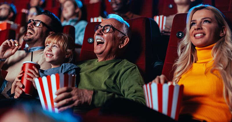 summer_movies A crowd of happy spectators are in the movie, sitting in the chairs laughing at the movie they are watching and enjoying popcorn and drinks.
