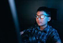 How to Teach Your Kids About Online Piracy and Its Risks oung kid on the computer playing games, watching entertainment or browsing the online digital internet, wearing glasses and dark background theme