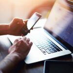 6 Tips for Recognizing Illegal Streaming Websites adult hands holding mobile phone over laptop keyboard