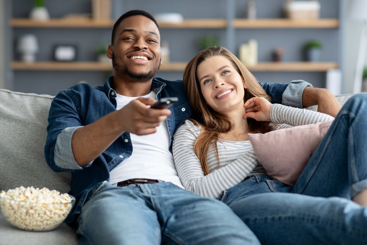 Streaming Oppenheimer on TV Couple sitting on couch with popcorn streaming Oppenheimer on TV