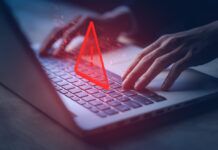 How Exactly Do Illegal Streaming Websites Work? Hands typing on a laptop with an icon of a warning label depicting illegal activities.
