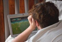 Is it Illegal to Use a VPN to Watch Sports? A young man laying on his bed watching an international soccer game on his laptop computer.