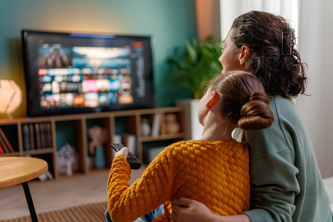 SafeStreaming_AllYear Happy family spending time together. Mother and child watching TV, movies in the evening at home.