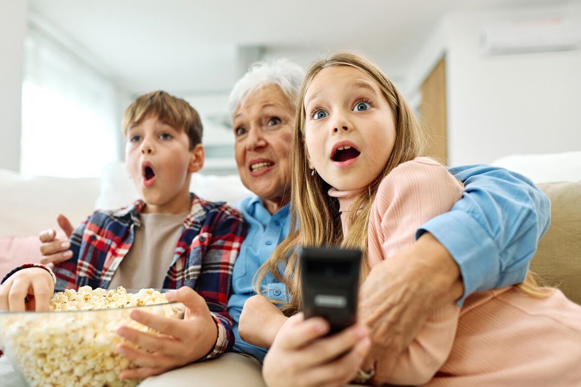 WhatIs_SafeStreaming2 Portrait of an elderly grandmother and grandchildren having fun watching tv together eating popcorn at home