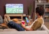 How to Safely Watch the 2026-27 NFL Regular Season Back view at young man watching football game at home and relaxing on couch with mobile streaming