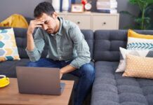 Beware of Illegal Sources: Rojadirecta Young man, looking stressed with his head in his hand, sits on couch and views his laptop screen after visiting an illegal streaming website